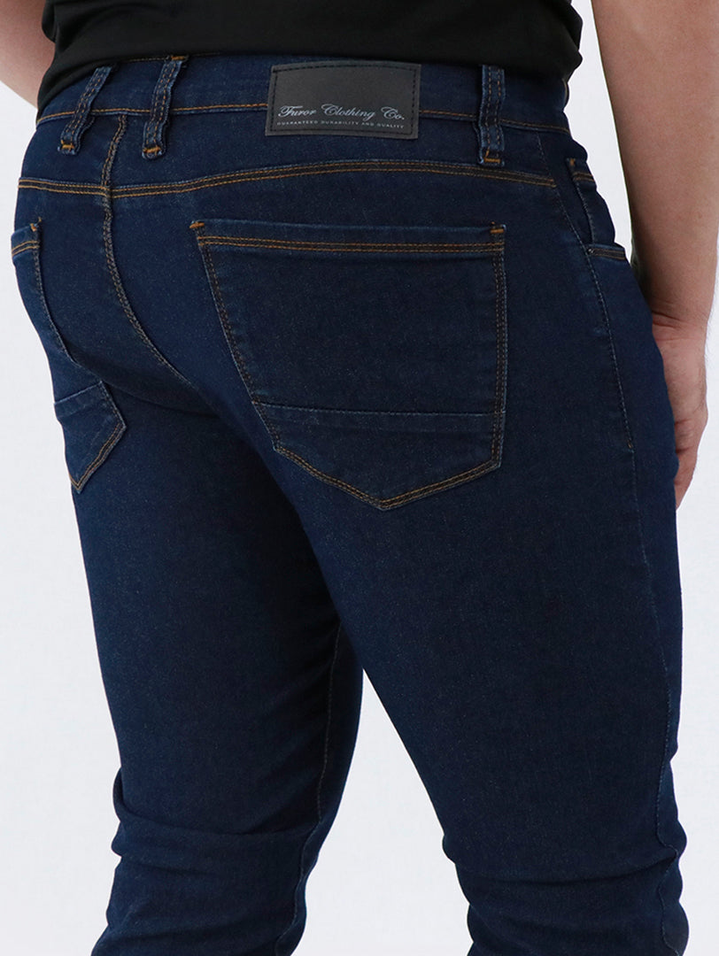 Detalle de pantalón de mezclilla azul oscuro para hombre con costuras en tono dorado.