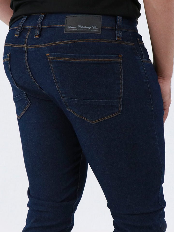 Detalle de pantalón de mezclilla azul oscuro para hombre con costuras en tono dorado.