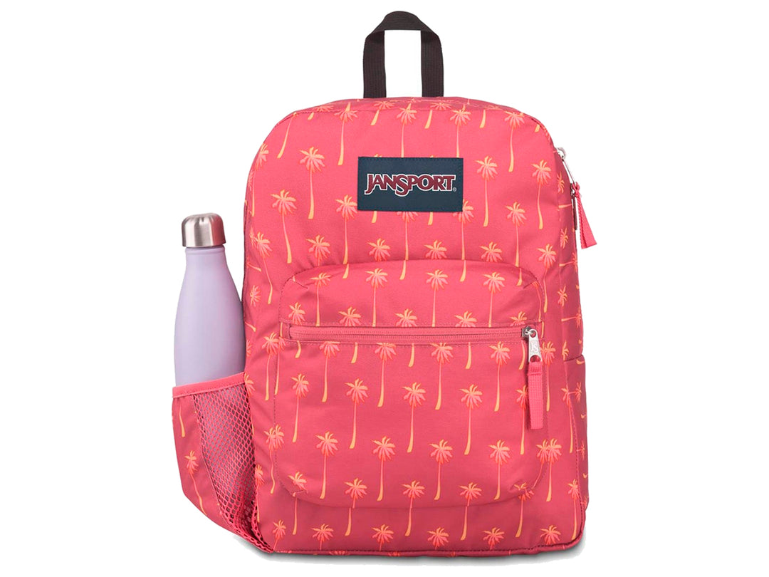 Mochila JanSport rosa con estampado de palmeras amarillas y un termo morado en el bolsillo lateral.