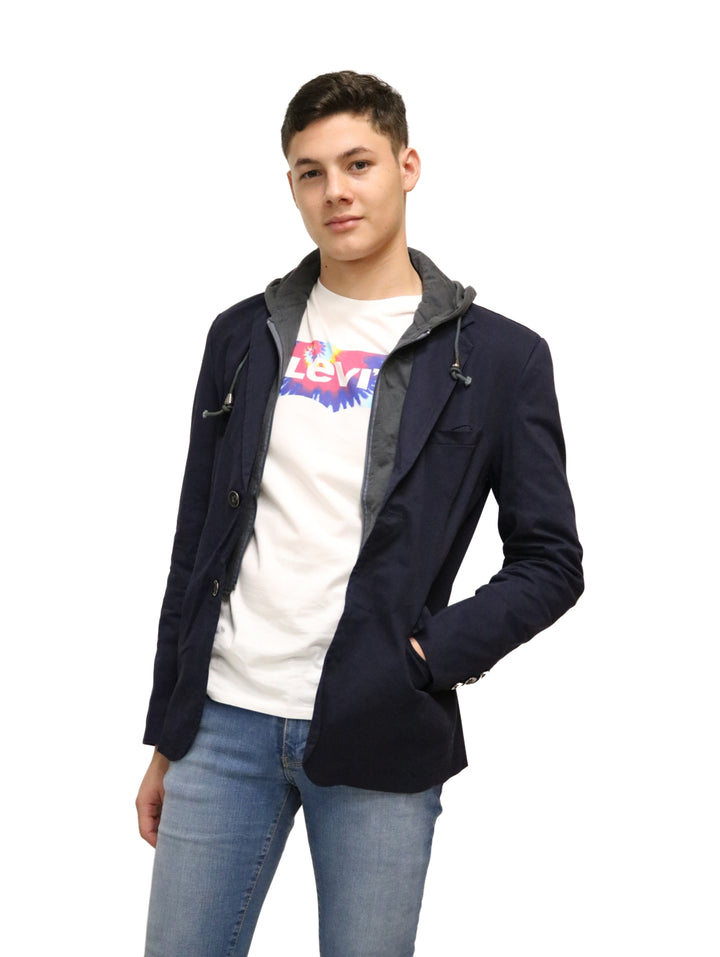 Hombre vistiendo un saco color marino con capucha gris, playera blanca y jeans azules.