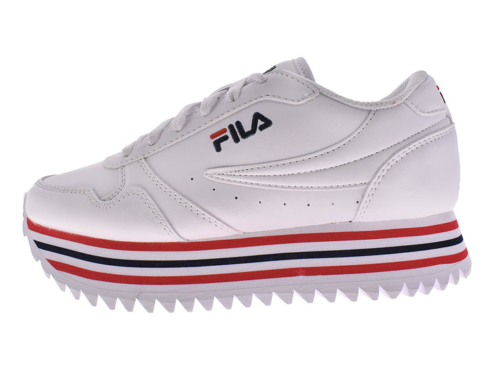 Tenis FILA blancos con detalles de rayas rojas y azules en la suela y base dentada.