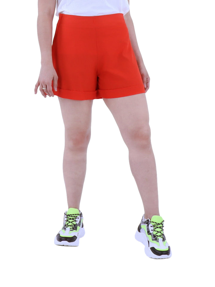 Mujer vistiendo short rojo de cintura alta con tenis deportivos sobre fondo blanco.