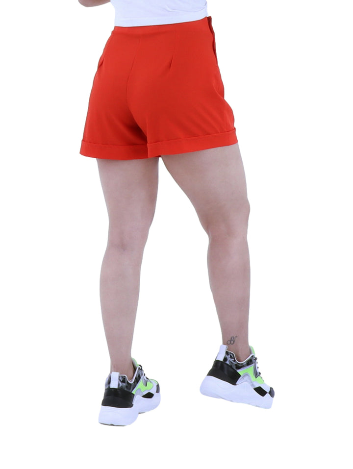 Mujer vistiendo short rojo de cintura alta con tenis deportivos sobre fondo blanco.