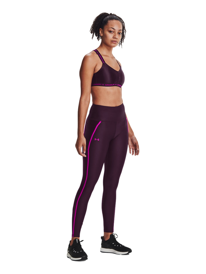 Mujer vistiendo mallas deportivas Under Armour color morado con franjas laterales en rosa brillante.