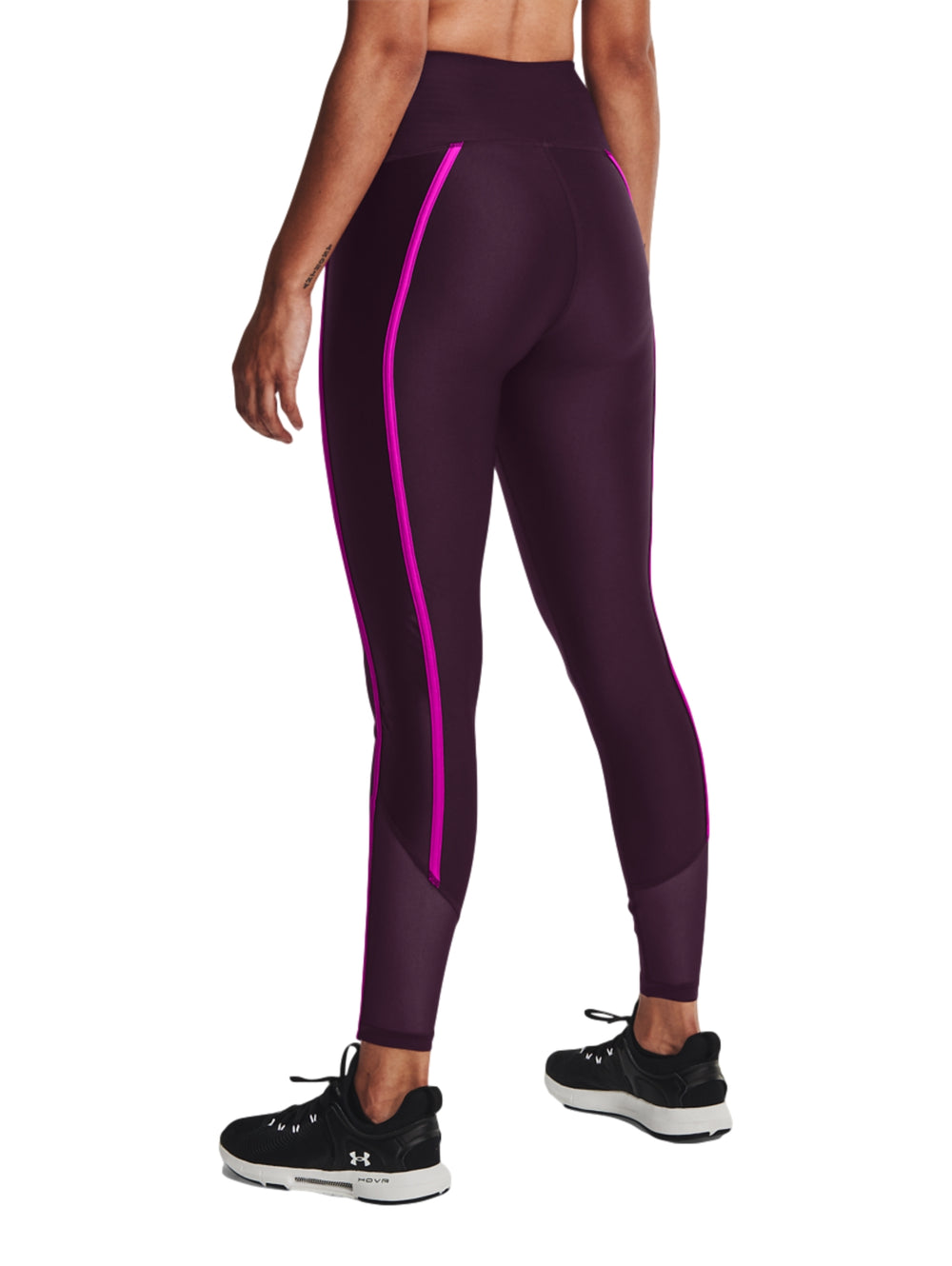 Mujer vistiendo mallas deportivas Under Armour color morado con franjas laterales en rosa brillante.