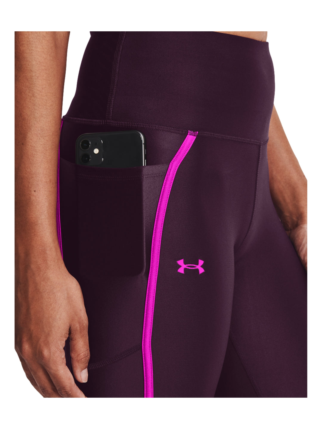 Mujer vistiendo mallas deportivas Under Armour color morado con franjas laterales en rosa brillante.