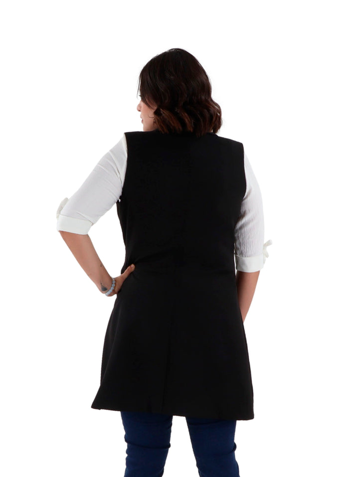 Mujer vistiendo un chaleco largo color negro con hebilla dorada en la cintura sobre una camisa blanca.