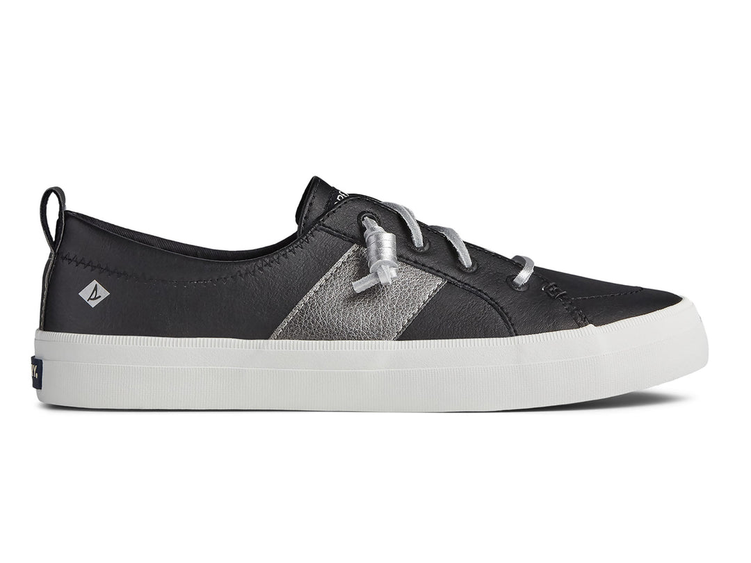 Zapato Sperry negro con franja plateada y suela blanca para mujer.