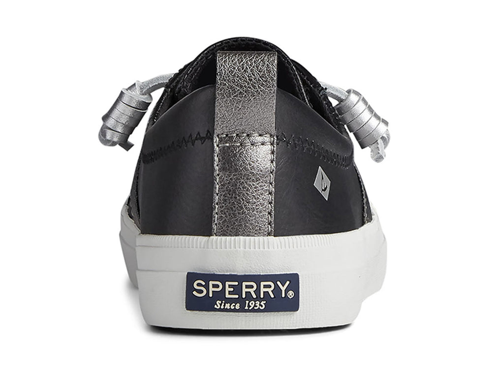 Zapato Sperry negro con franja plateada y suela blanca para mujer.