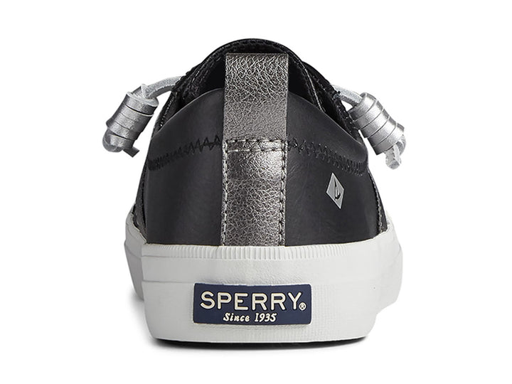 Zapato Sperry negro con franja plateada y suela blanca para mujer.