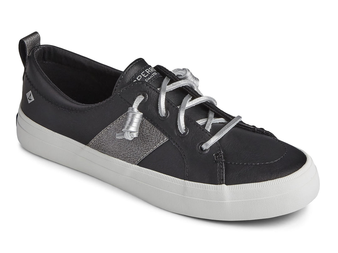 Zapato Sperry negro con franja plateada y suela blanca para mujer.