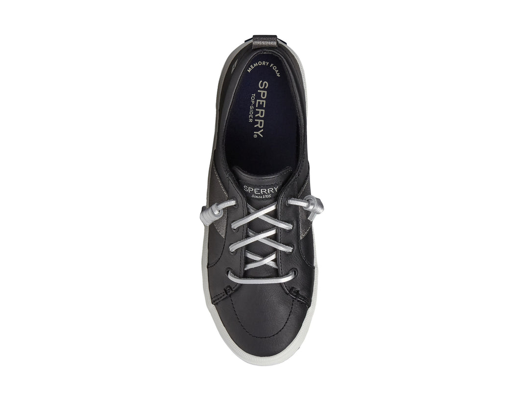 Zapato Sperry negro con franja plateada y suela blanca para mujer.