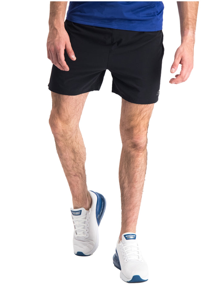 Hombre vistiendo short deportivo color negro de la marca Skechers con camiseta azul y tenis blancos.