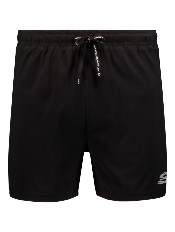 Hombre vistiendo short deportivo color negro de la marca Skechers con camiseta azul y tenis blancos.