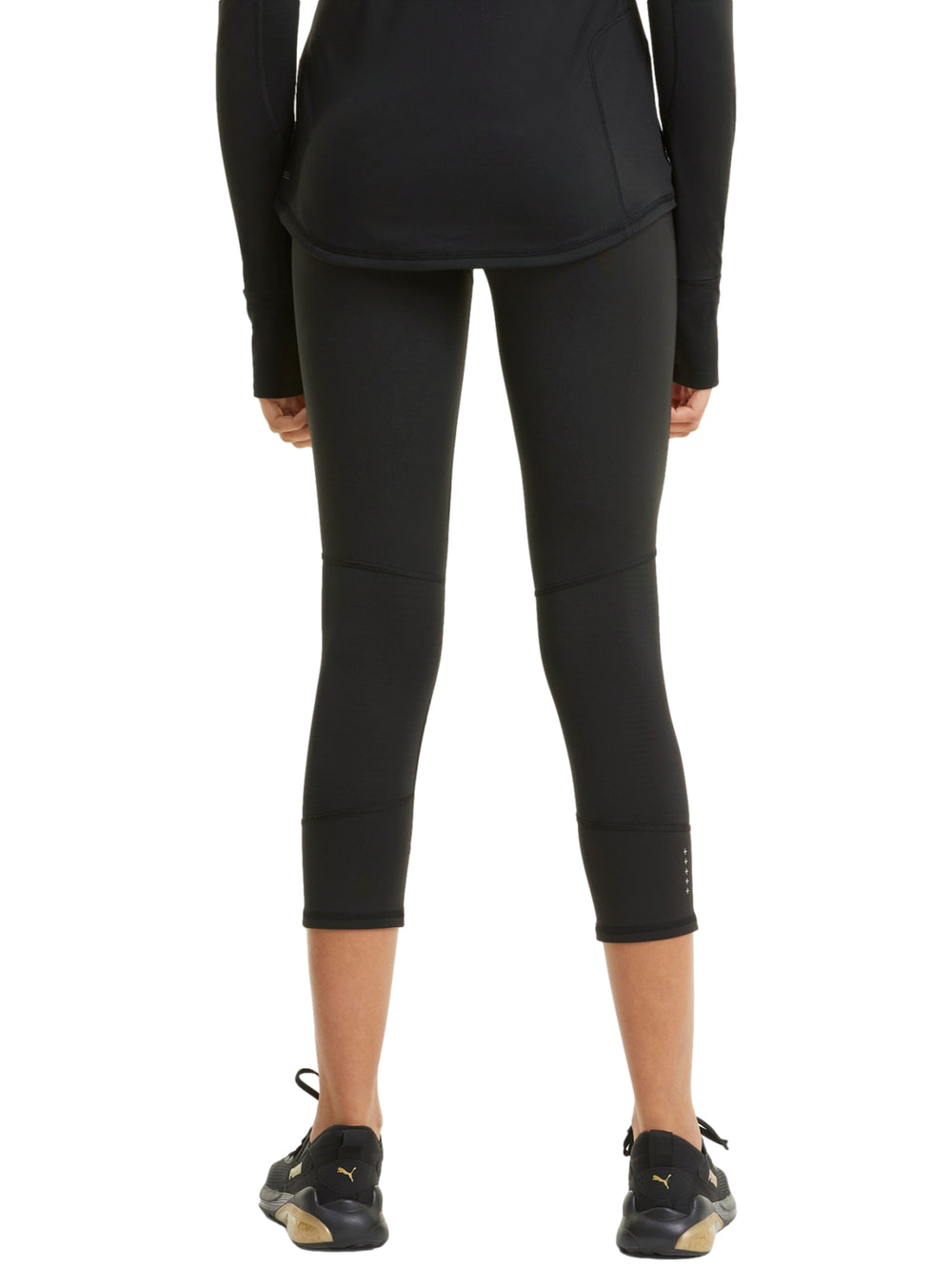 Mujer vistiendo mallas deportivas PUMA de color negro, longitud 3/4, ajustadas al cuerpo.