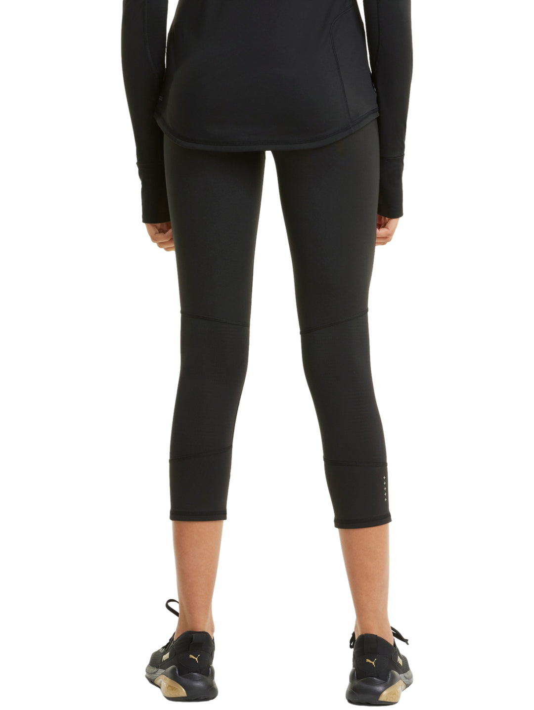 Mujer vistiendo mallas deportivas PUMA de color negro, longitud 3/4, ajustadas al cuerpo.