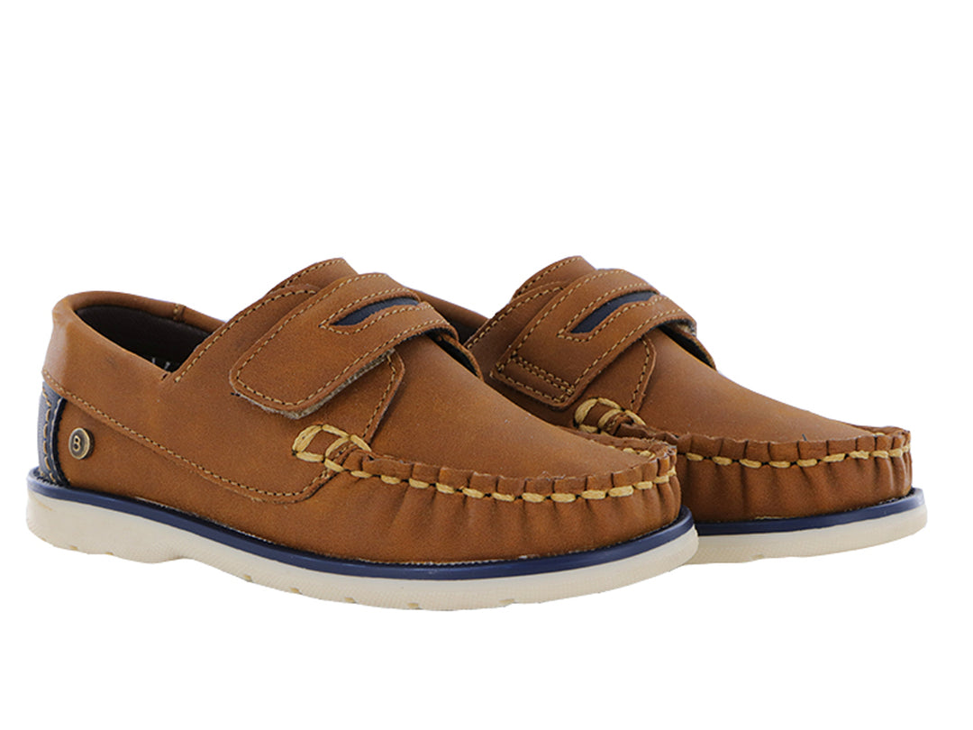 Zapatos tipo mocasín color tan para niño con correa ajustable y suela blanca con detalle azul.