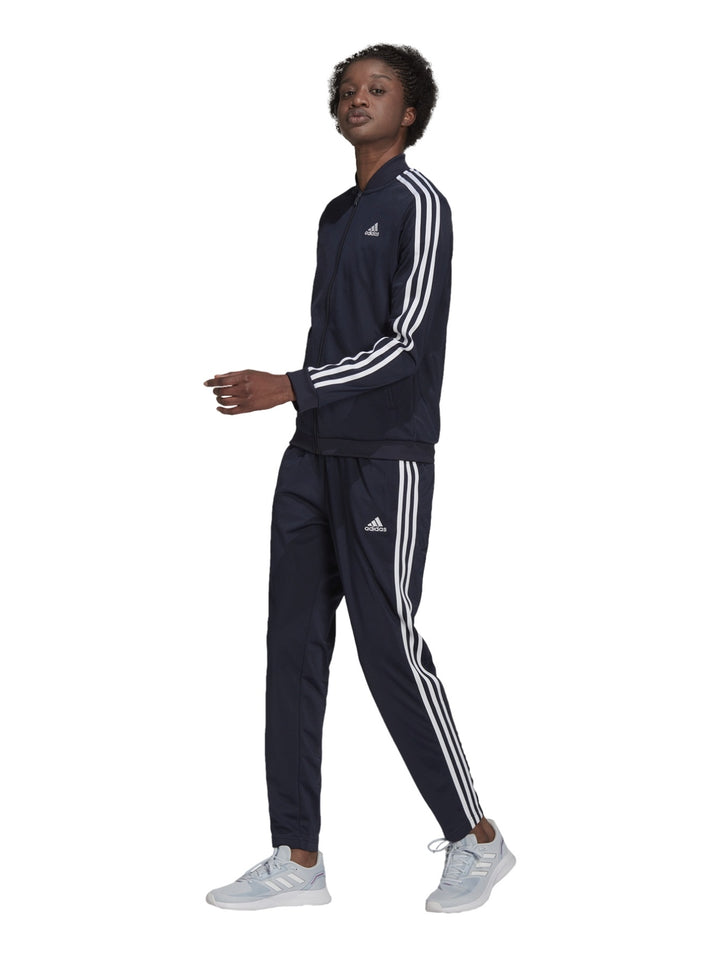 Mujer vistiendo conjunto deportivo Adidas azul marino oscuro con rayas blancas laterales.