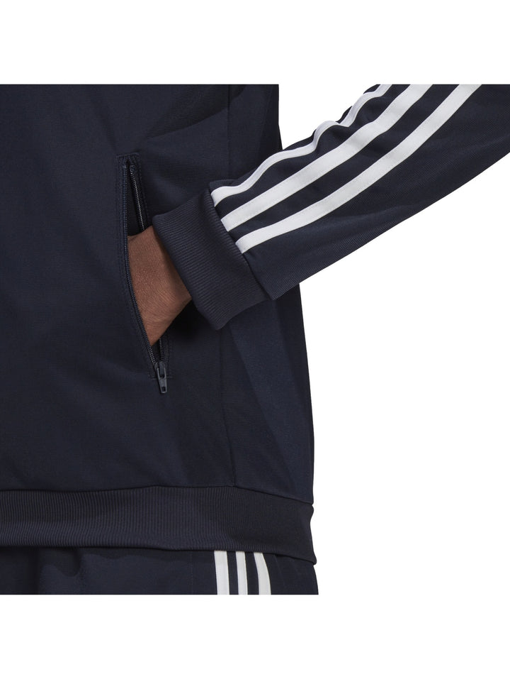 Mujer vistiendo conjunto deportivo Adidas azul marino oscuro con rayas blancas laterales.