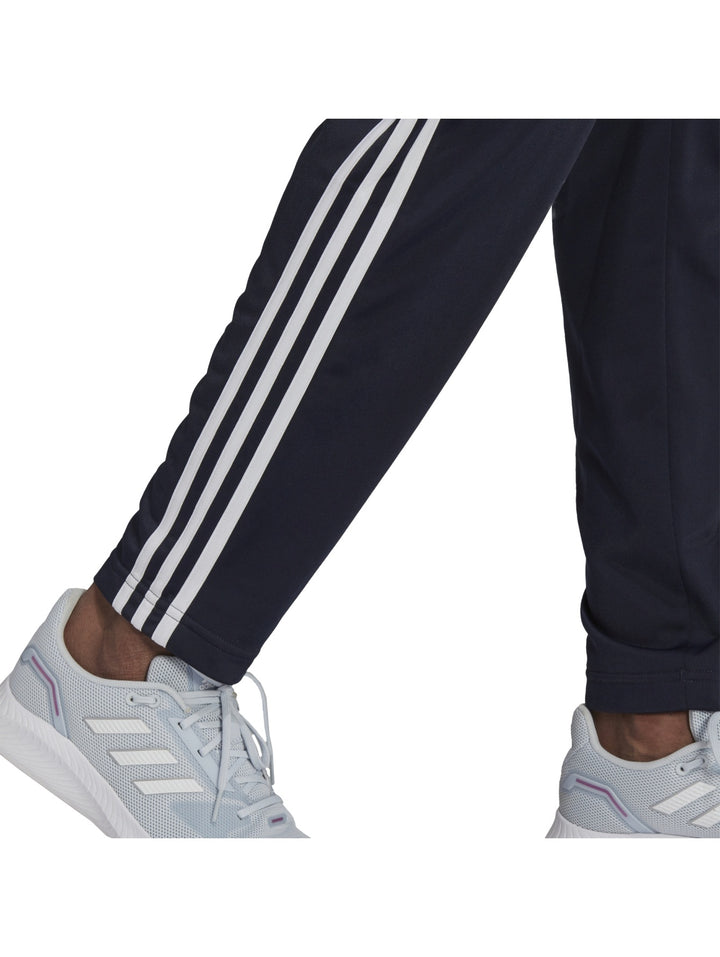 Mujer vistiendo conjunto deportivo Adidas azul marino oscuro con rayas blancas laterales.