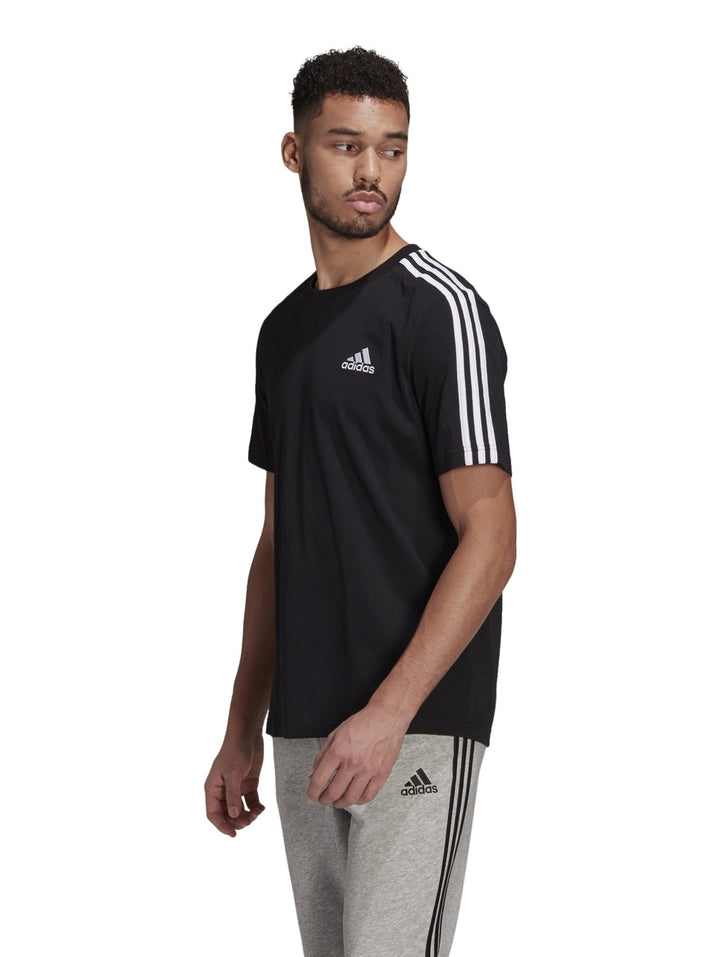 Hombre vistiendo playera deportiva Adidas color negro con tres franjas blancas en los hombros.