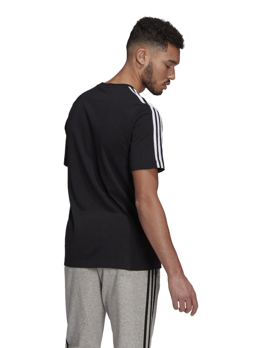 Hombre vistiendo playera deportiva Adidas color negro con tres franjas blancas en los hombros.
