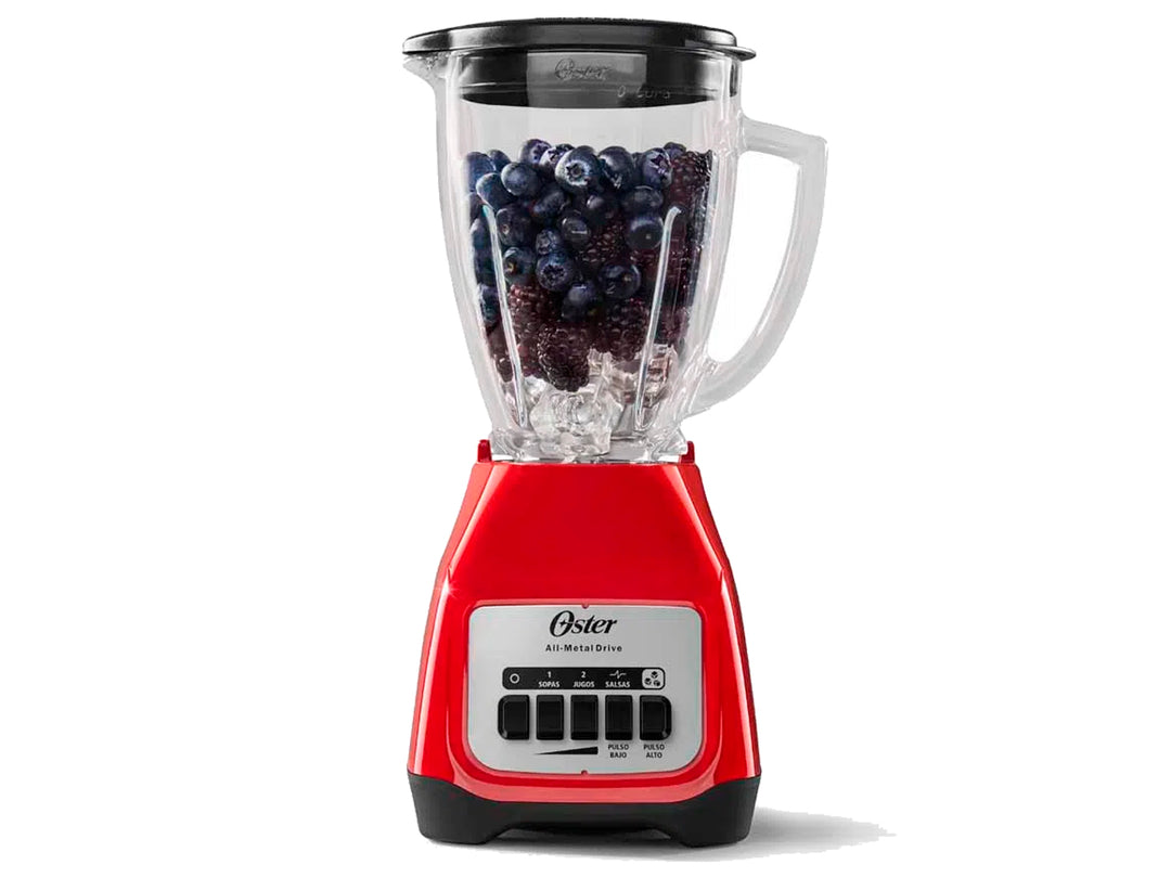 Licuadora Oster de color rojo con vaso de vidrio transparente lleno de arándanos y hielo.
