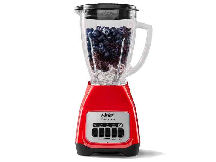 Licuadora Oster de color rojo con vaso de vidrio transparente lleno de arándanos y hielo.