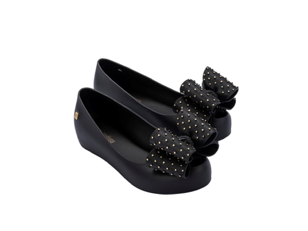 Zapatos planos negros para niña con moño decorado con puntos dorados.