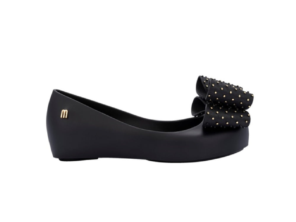 Zapatos planos negros para niña con moño decorado con puntos dorados.