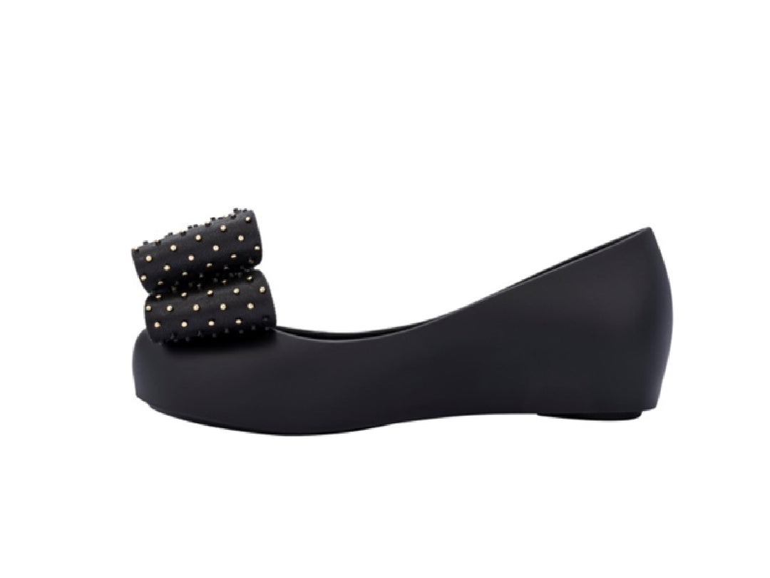Zapatos planos negros para niña con moño decorado con puntos dorados.
