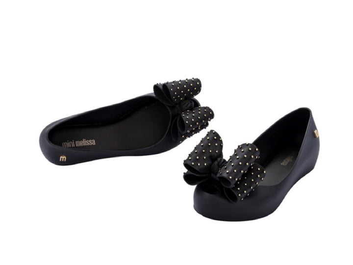 Zapatos planos negros para niña con moño decorado con puntos dorados.