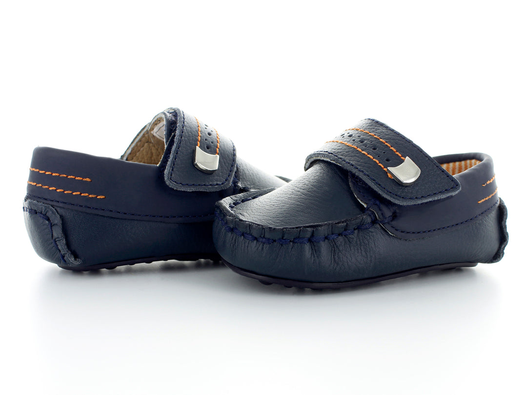 Par de zapatos tipo mocasín color azul marino para bebé con costuras decorativas en naranja y hebilla plateada.