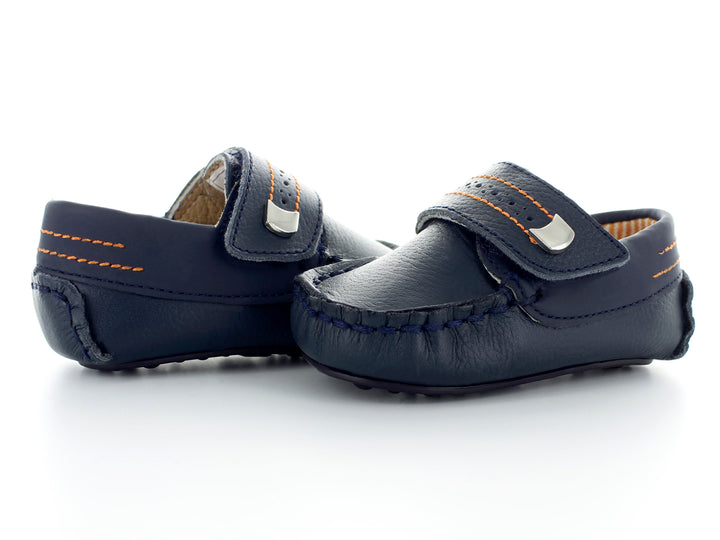 Par de zapatos tipo mocasín color azul marino para bebé con costuras decorativas en naranja y hebilla plateada.