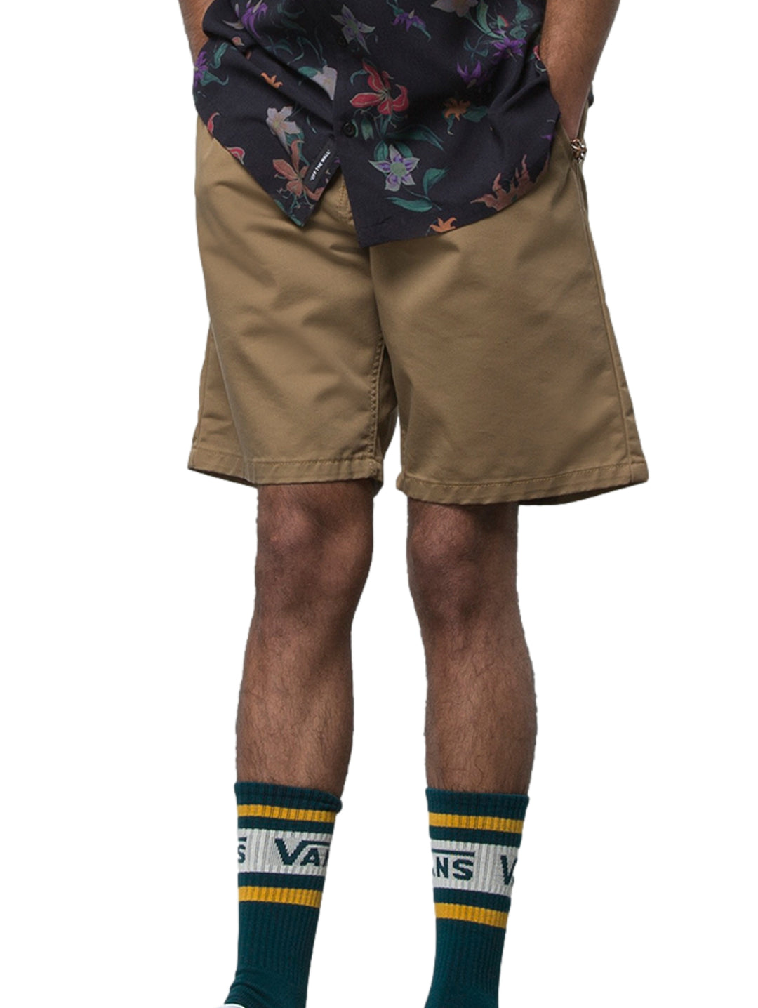 Hombre usando pantalones cortos color café marca Vans, calcetines verdes y camisa oscura floral.