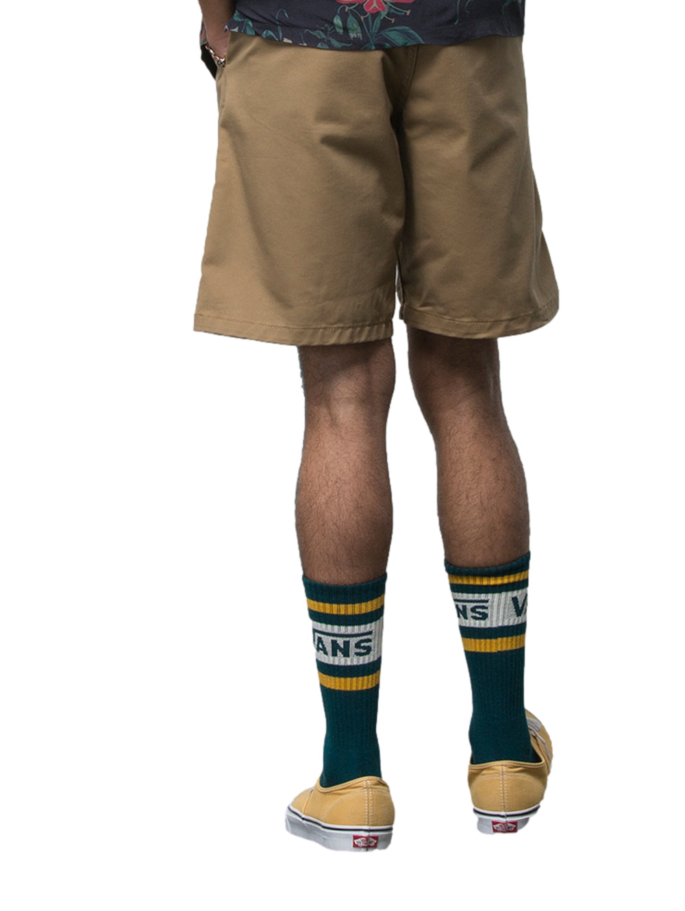Hombre usando pantalones cortos color café marca Vans, calcetines verdes y camisa oscura floral.