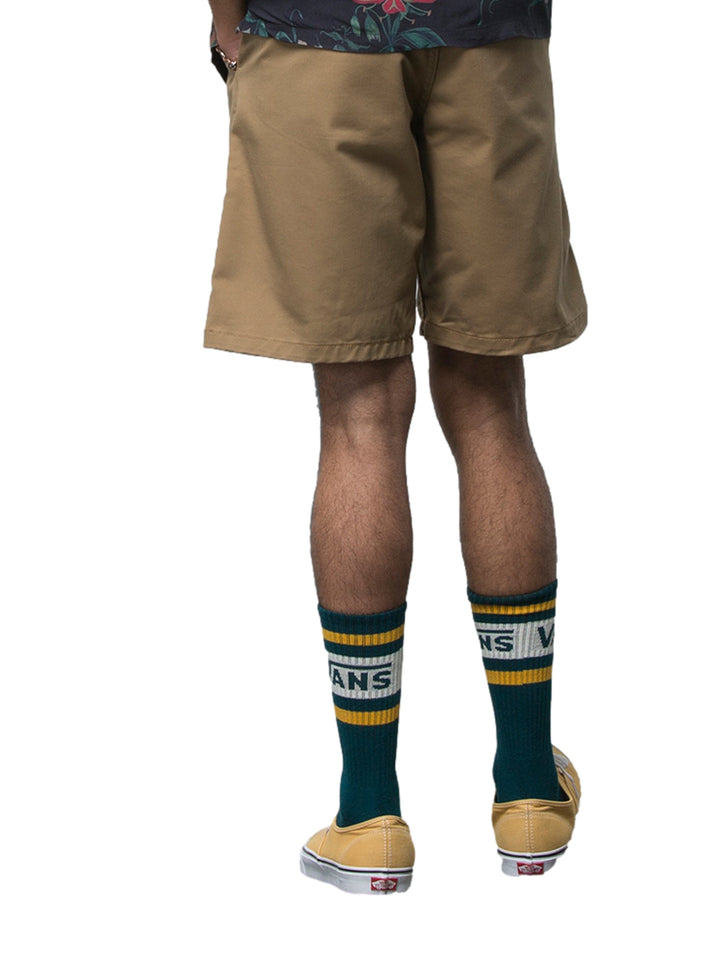 Hombre usando pantalones cortos color café marca Vans, calcetines verdes y camisa oscura floral.