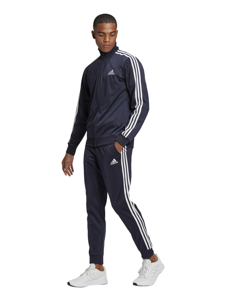 Hombre vistiendo conjunto deportivo Adidas azul marino con tres franjas blancas laterales.