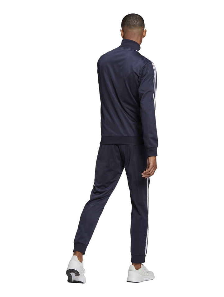 Hombre vistiendo conjunto deportivo Adidas azul marino con tres franjas blancas laterales.