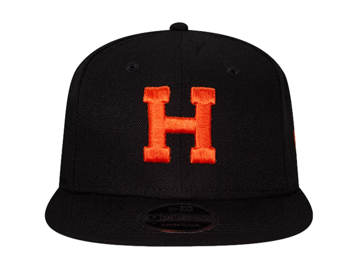Gorra de béisbol New Era color negro con letra H bordada en naranja y visera plana.