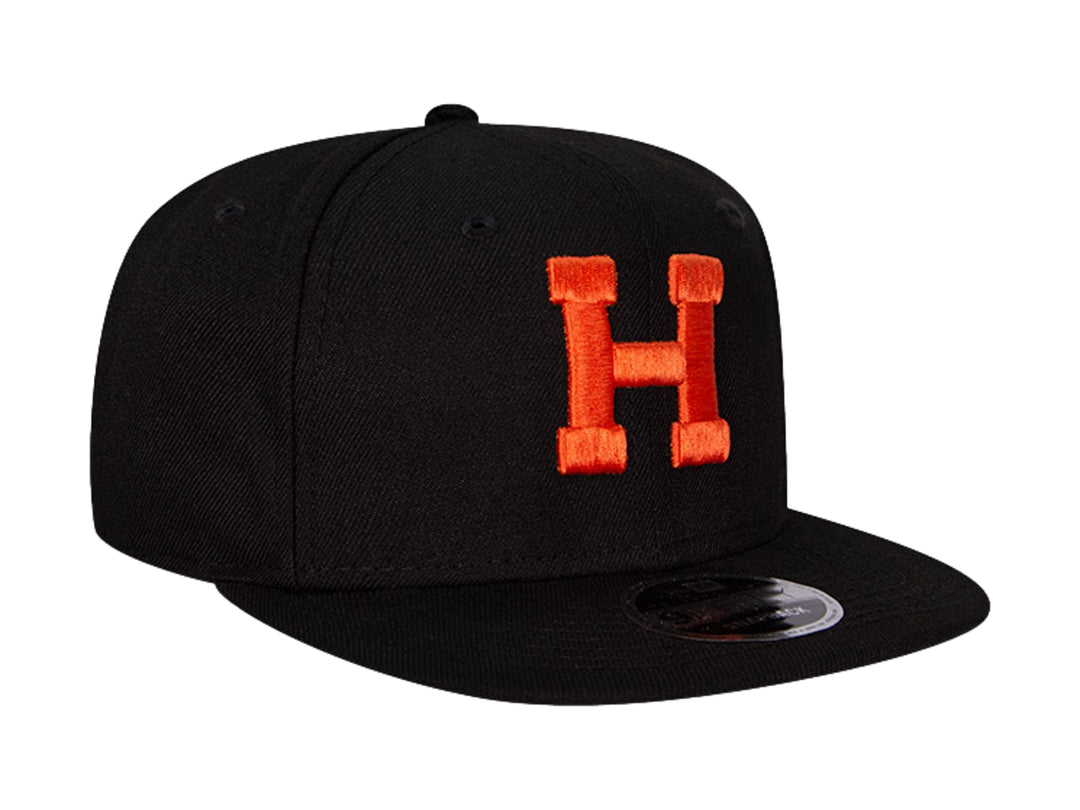 Gorra de béisbol New Era color negro con letra H bordada en naranja y visera plana.