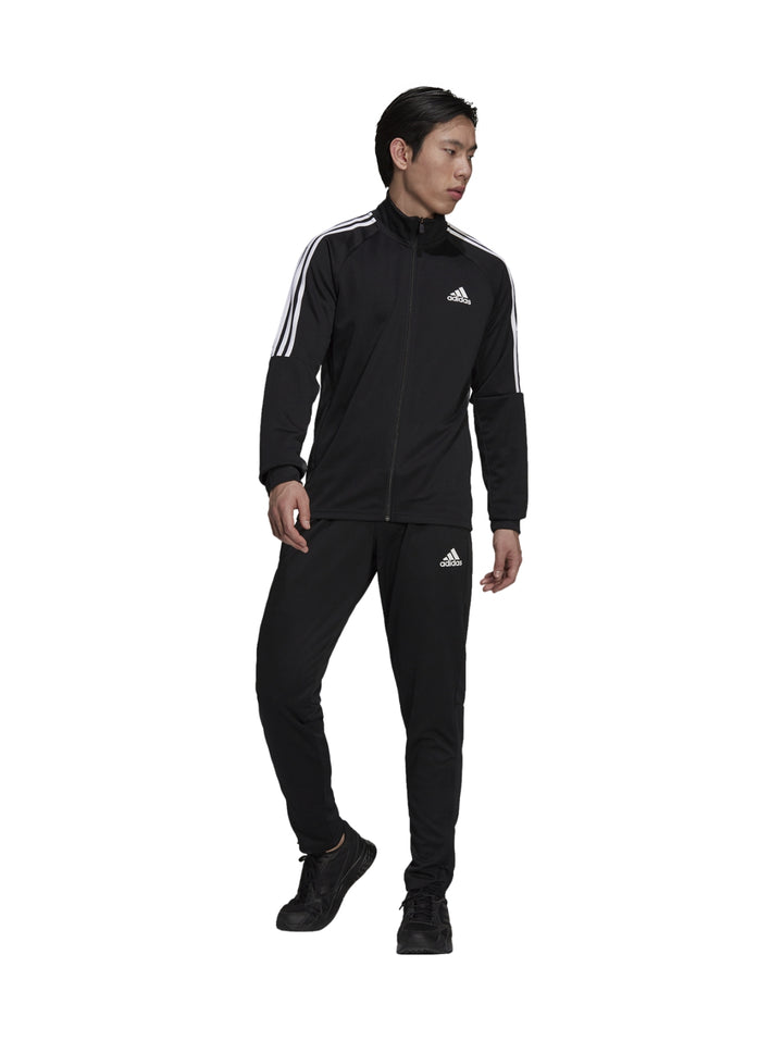 Hombre vistiendo conjunto deportivo Adidas de color negro con rayas blancas en las mangas.