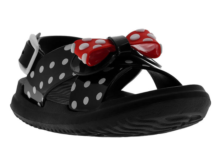 Sandalia negra brillante para niña con moño rojo y blanco con lunares y tiras decoradas con puntos blancos.