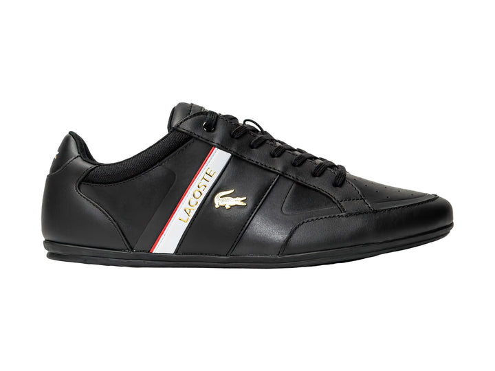 Tenis Lacoste color negro con franja blanca y roja lateral y logotipo del cocodrilo.