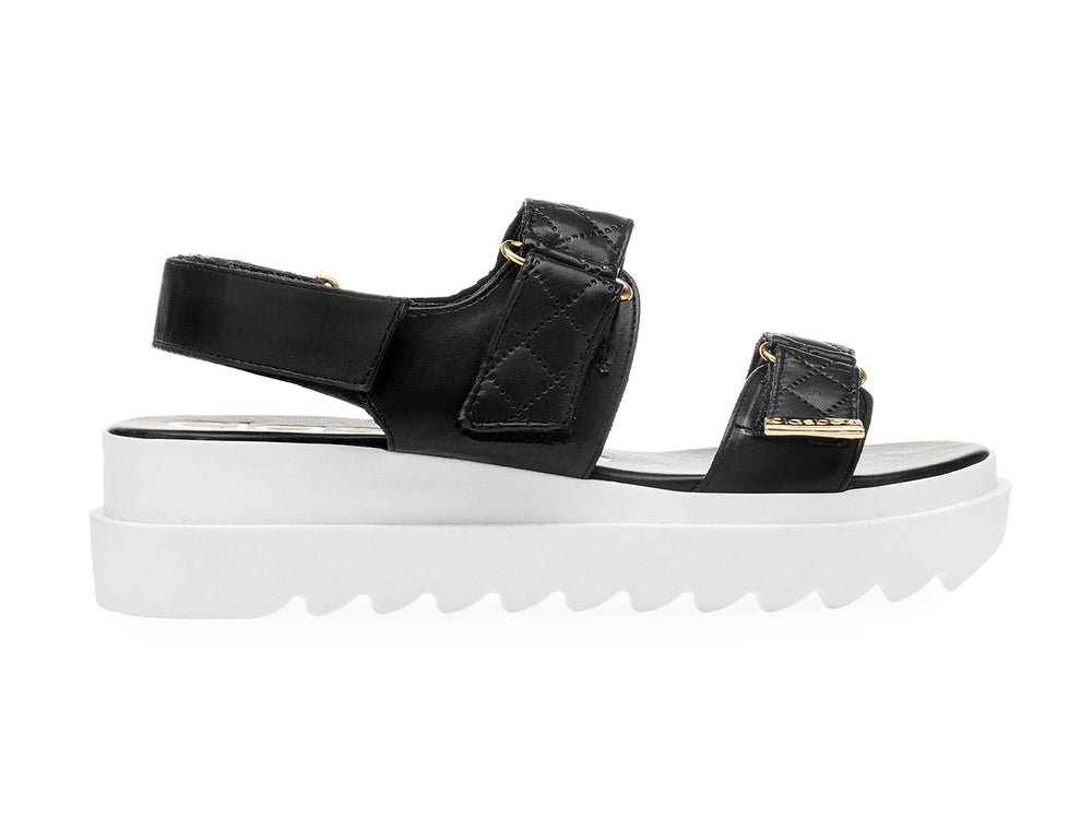 Sandalia negra de plataforma blanca con correas acolchadas y hebillas doradas para mujer.