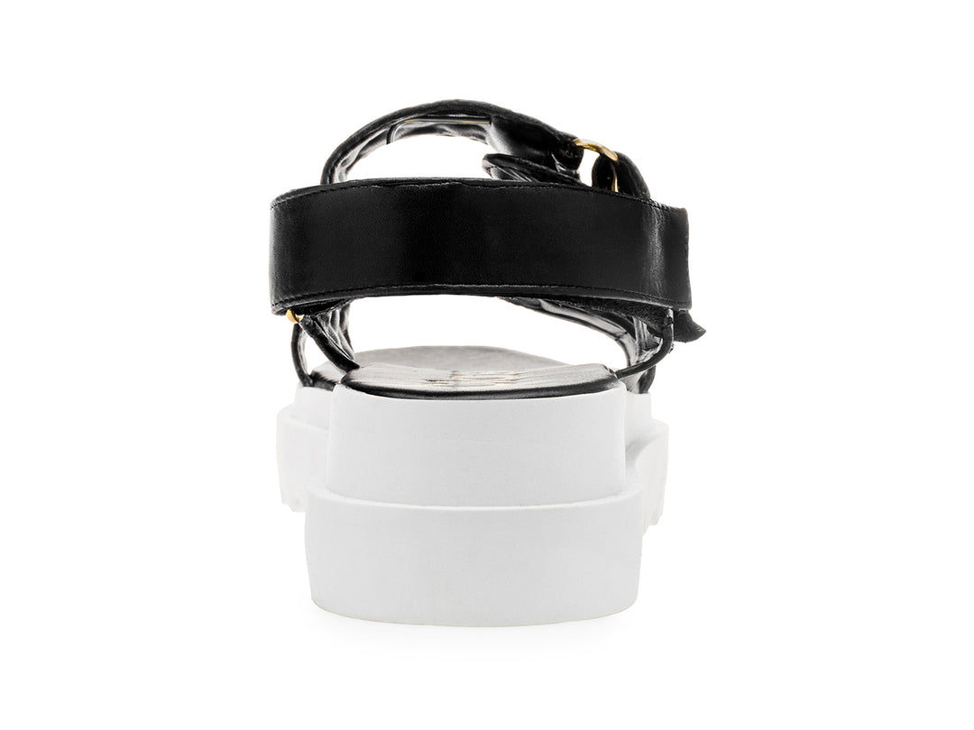 Sandalia negra de plataforma blanca con correas acolchadas y hebillas doradas para mujer.