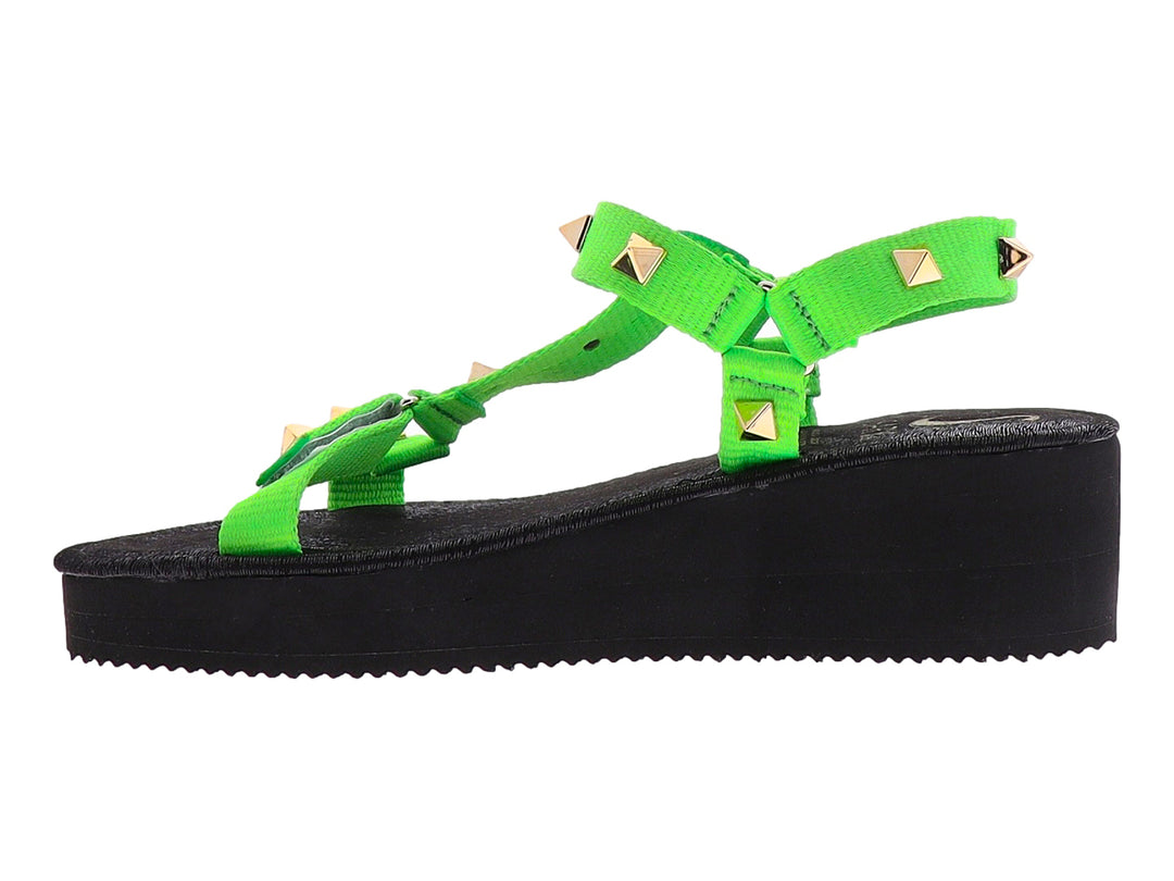 Sandalia de plataforma negra con tiras verde neón y tachuelas doradas.
