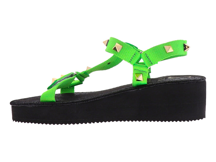 Sandalia de plataforma negra con tiras verde neón y tachuelas doradas.