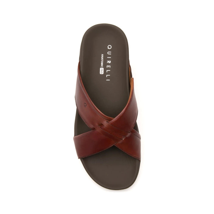 Sandalia plana de cuero color vino con diseño de tiras cruzadas y suela negra.