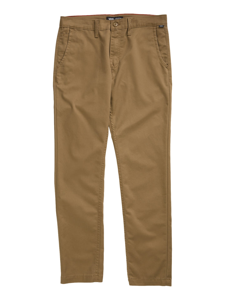 Hombre vistiendo pantalón chino color café marca Vans con camiseta blanca y tenis a cuadros.